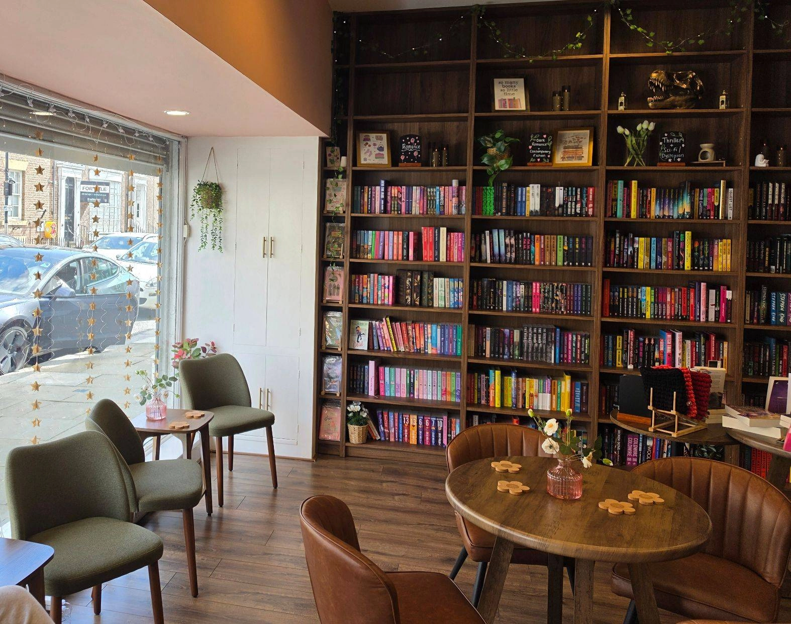 Chapter 13 bookshop and tearoom interior with a book wall, window seating, wooden tables and green chairs.